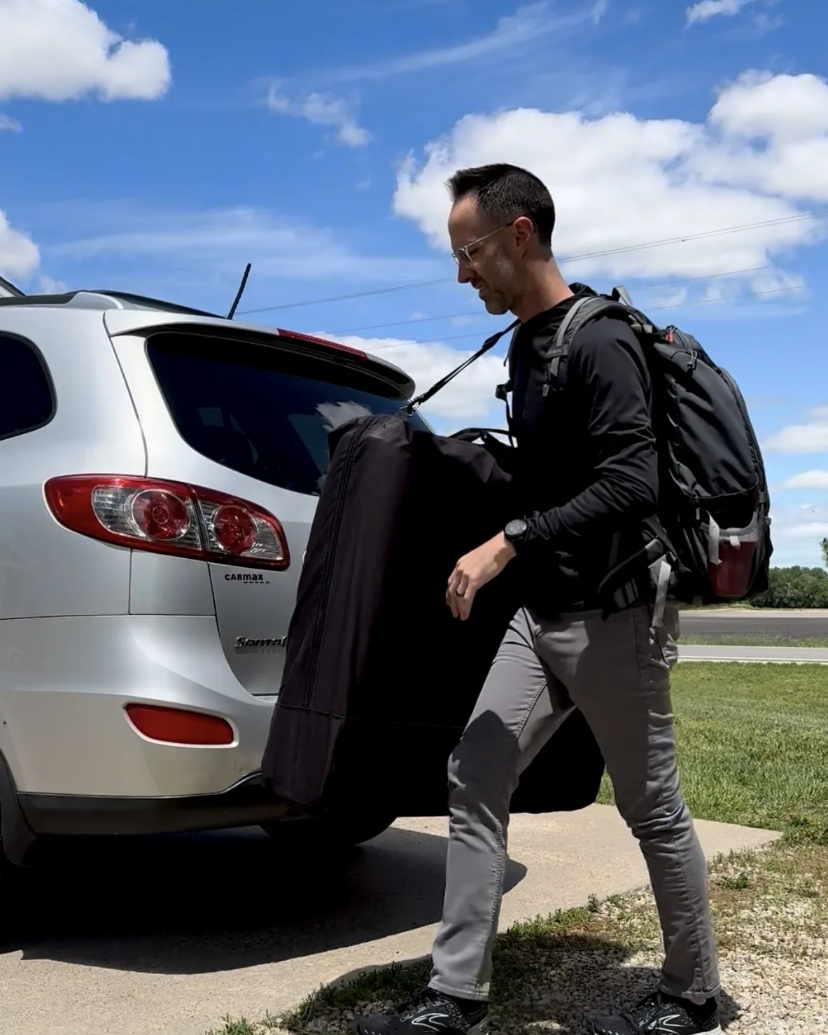 Dr. Travis Nichols lifting his folded treatment table out of the back of his car, bag on his shoulder, on the way to a visit